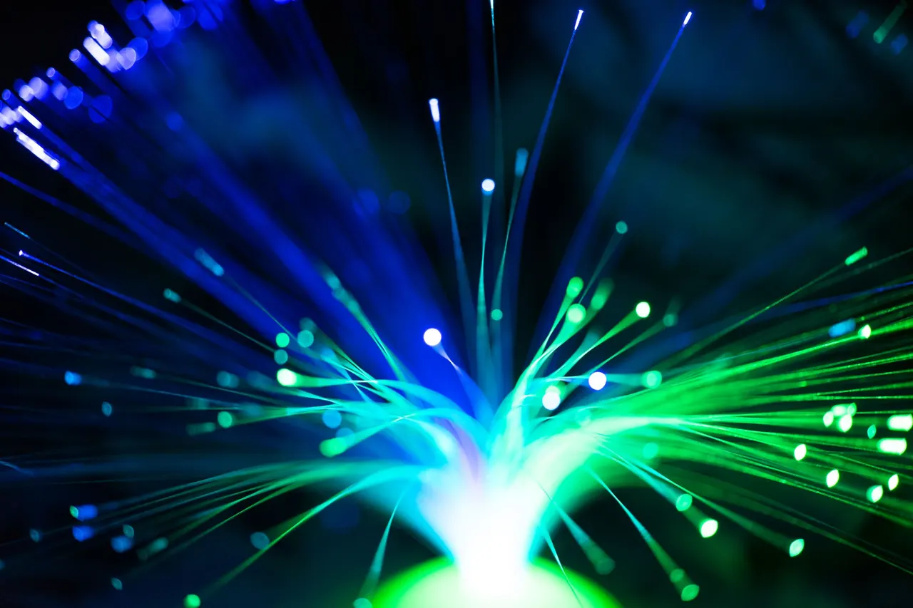 Berkas kabel fiber optic yang memancarkan cahaya oranye dan biru.